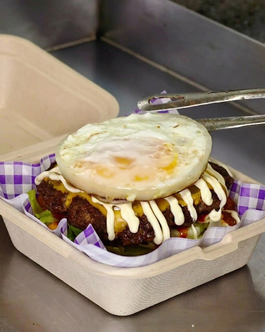 Colocando un huevo frito recién hecho sobre la hamburguesa con todos sus ingredientes y mayonesa.