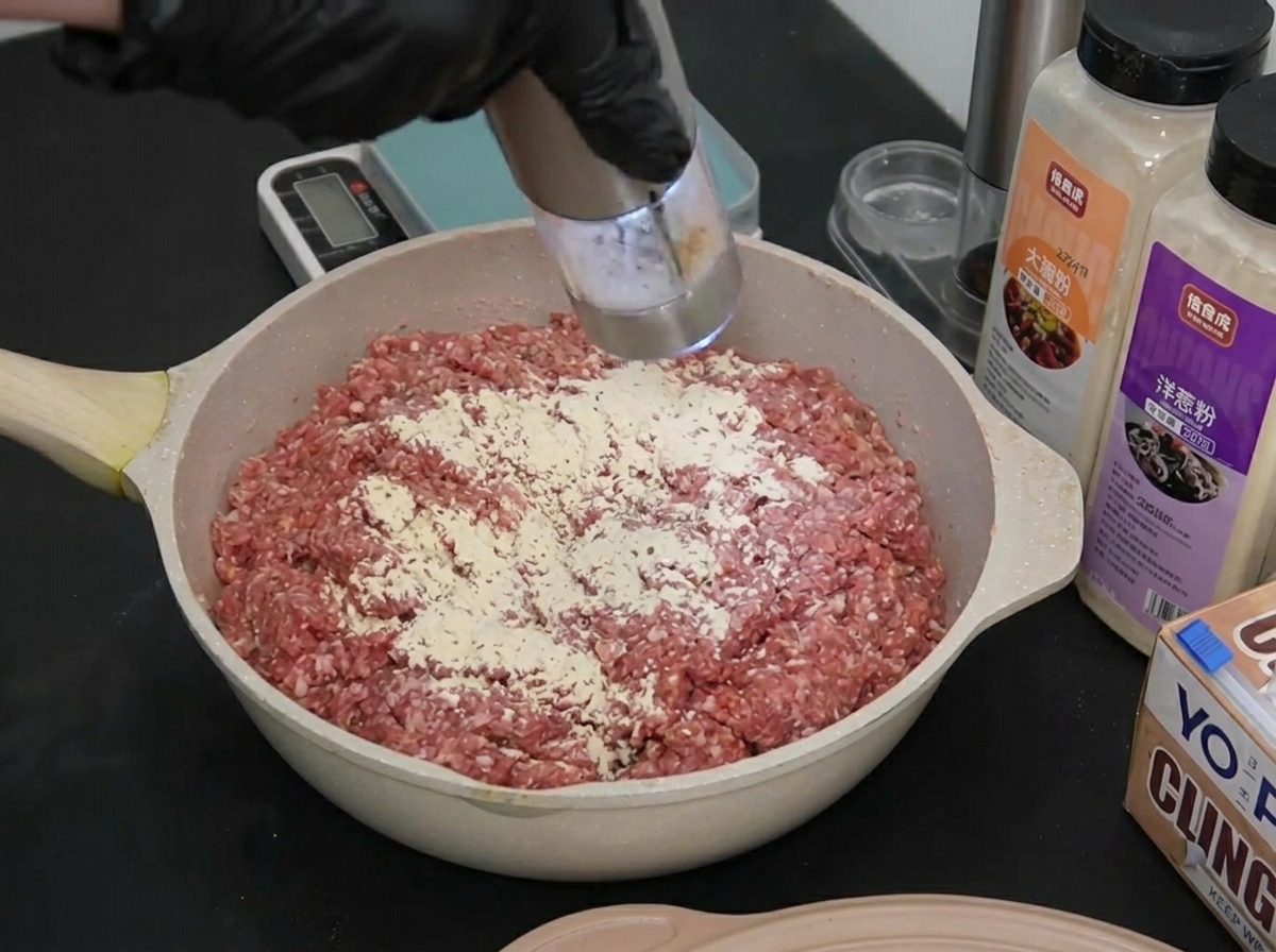 Una mano con guante moliendo una pequeña cantidad de sal marina blanca sobre la superficie de la carne sazonada.