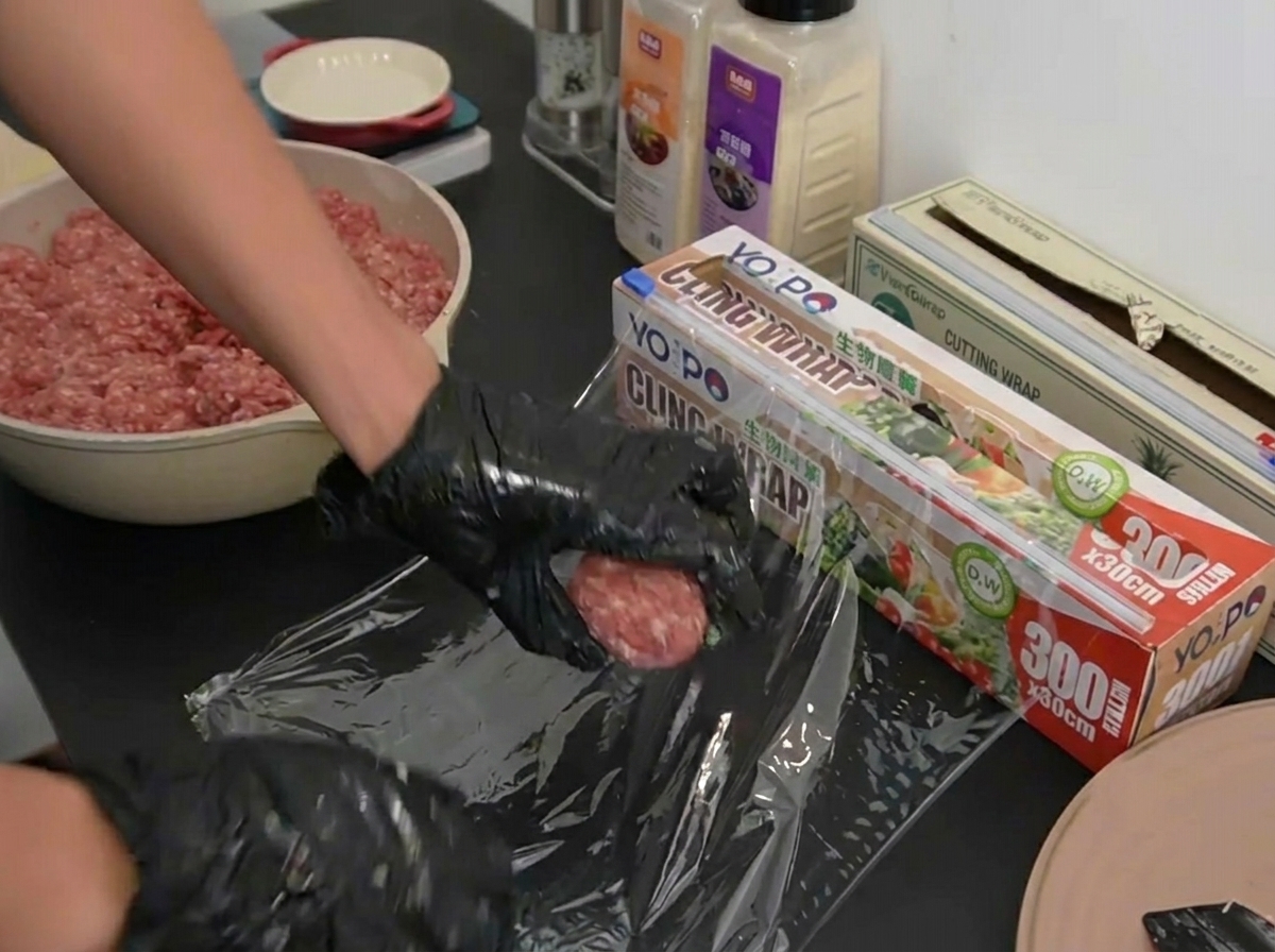 Manos con guantes colocando una bola de carne perfectamente porcionada sobre una lámina de papel film.