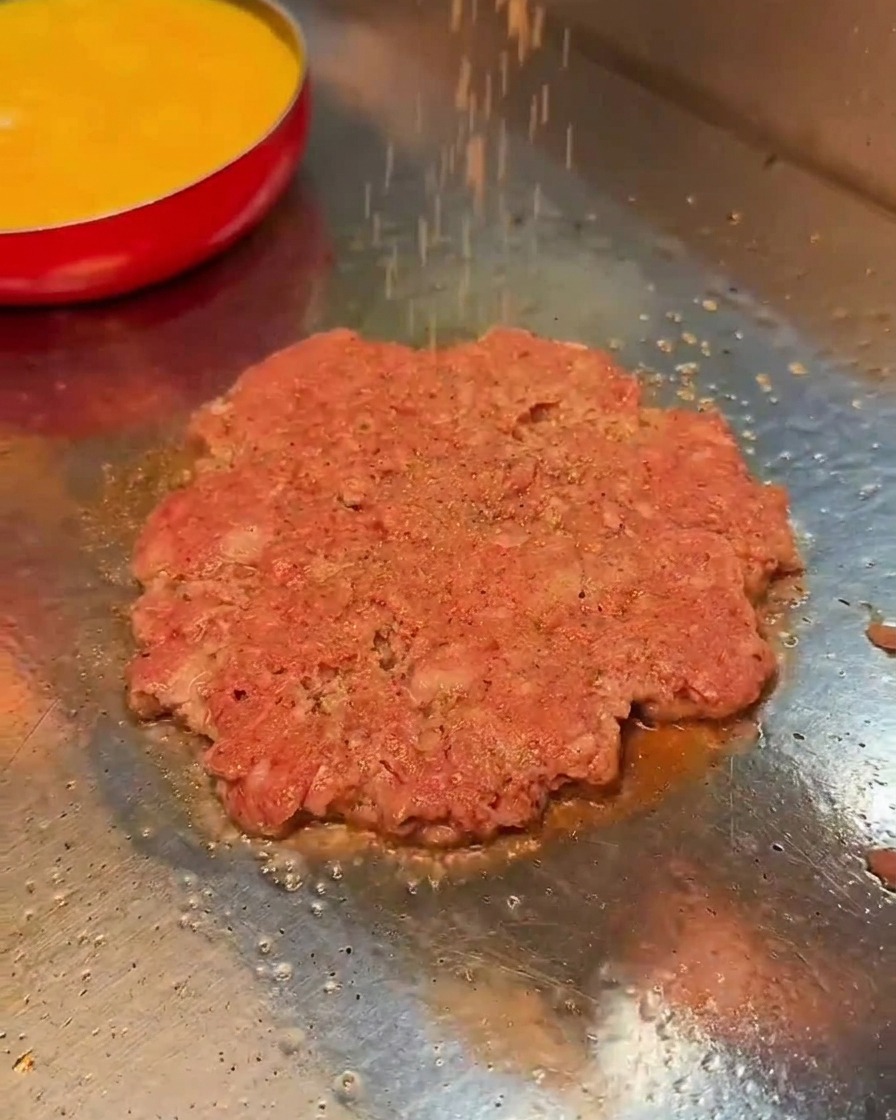 Sal y pimienta negra siendo espolvoreadas sobre la carne en la plancha.