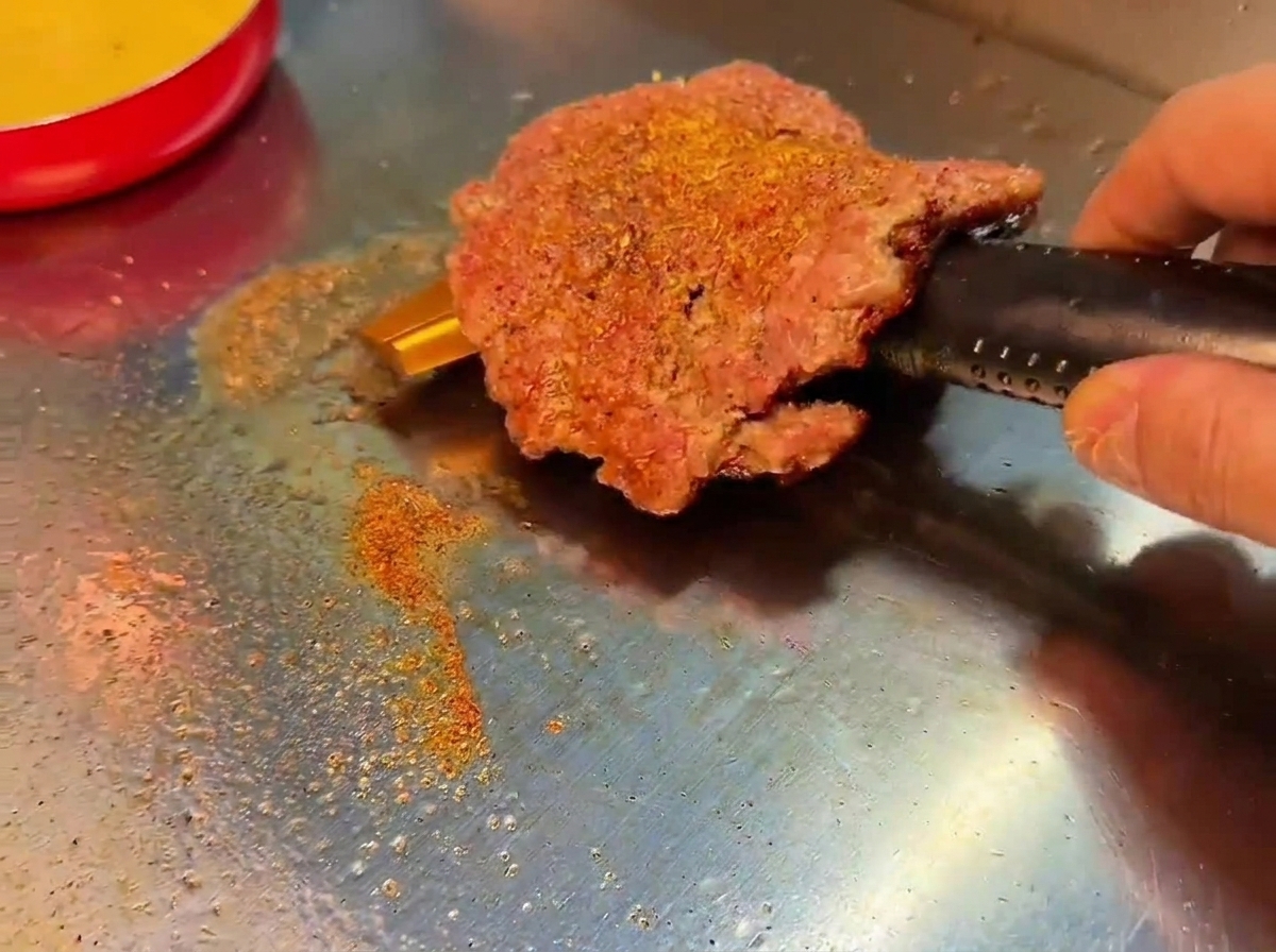 Una hamburguesa smash a la que se le da la vuelta revelando una costra marrón oscura y caramelizada.