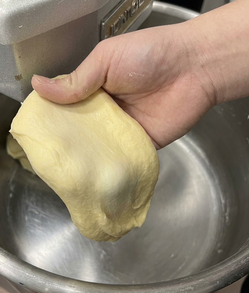 Una mano estirando una porción de masa de brioche para mostrar la membrana fina y resistente.