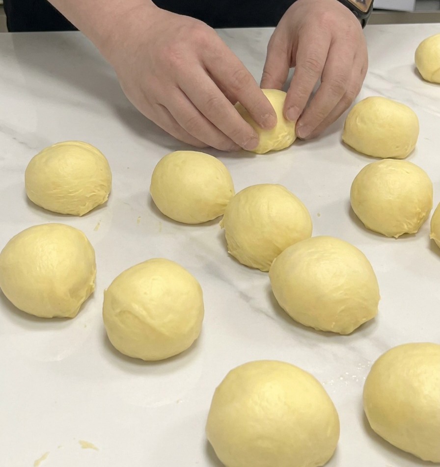 Manos dando forma de bola a porciones de masa de brioche sobre una encimera de mármol.