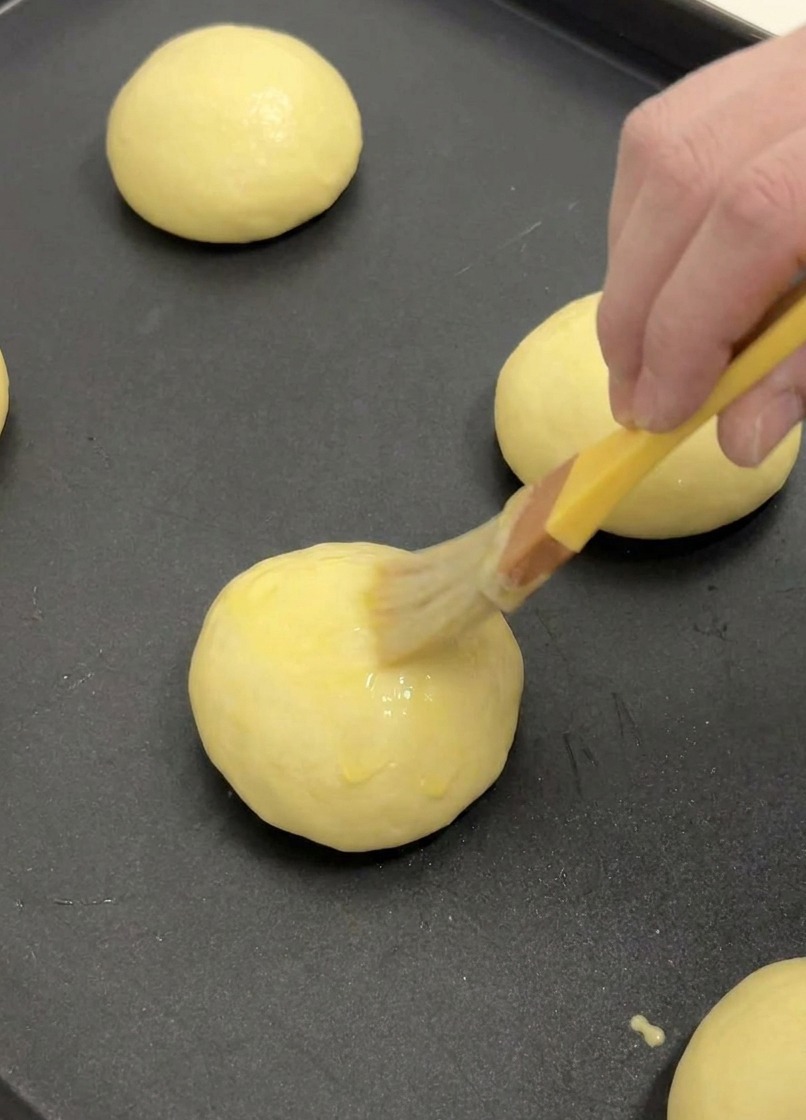 Pincel de cocina aplicando una capa de huevo batido sobre un bollo de brioche fermentado.