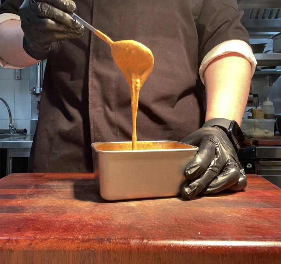 Una mano levantando una cuchara con salsa de color naranja vibrante desde un bol.