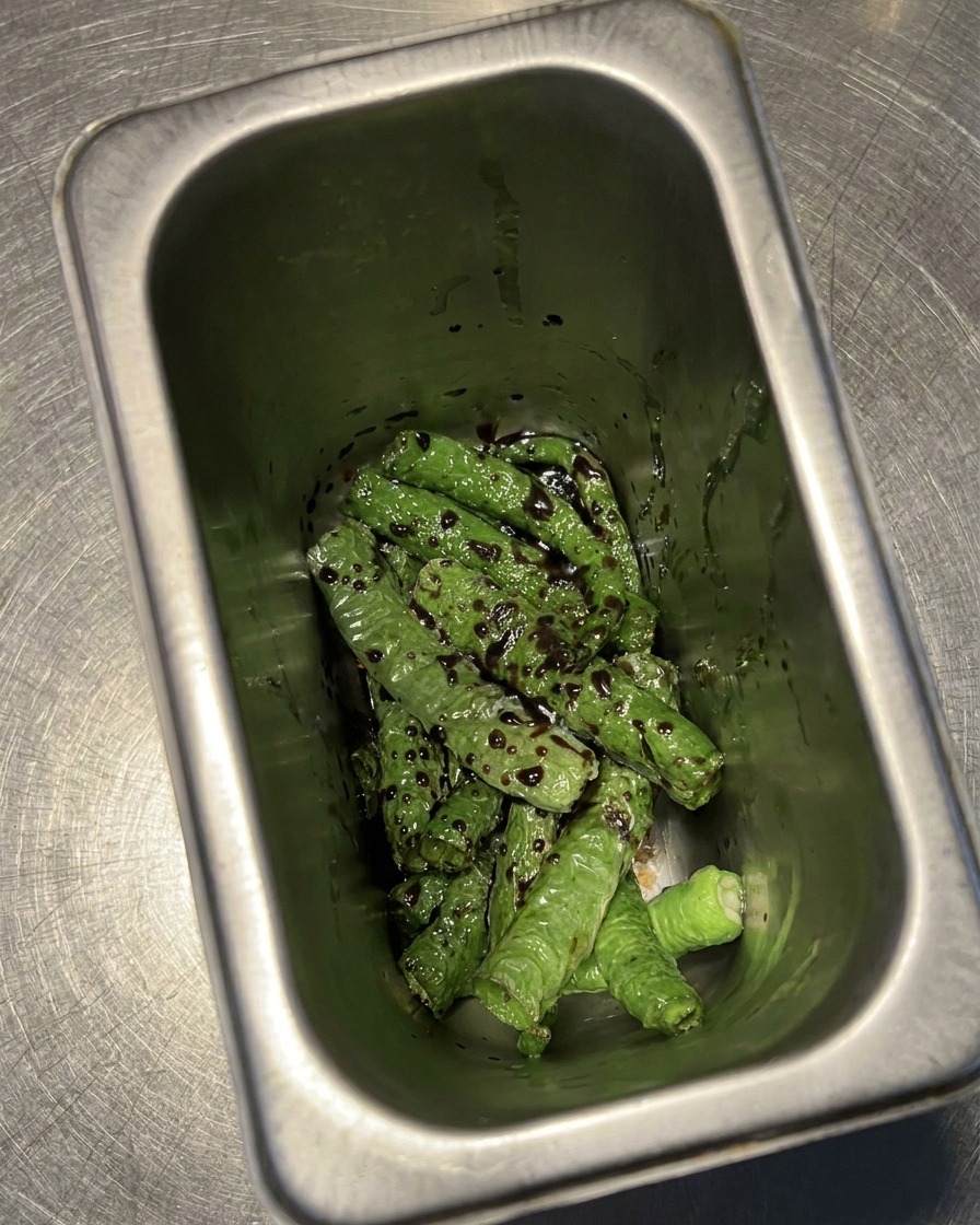 Chiles fritos en un recipiente metálico bañados en una mezcla oscura de vinagre y soja.