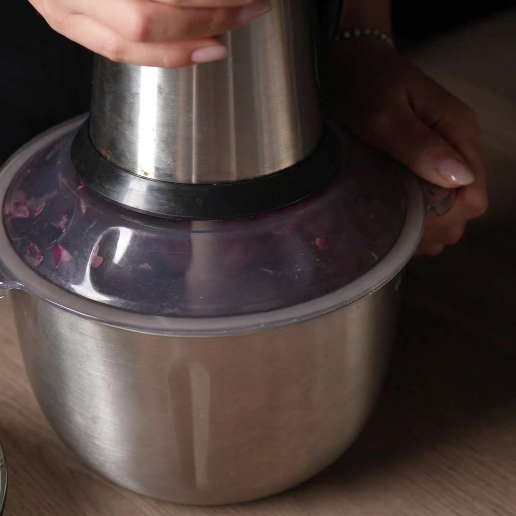 Una mano presionando la tapa de un procesador de alimentos para picar la mezcla de carne cruda.
