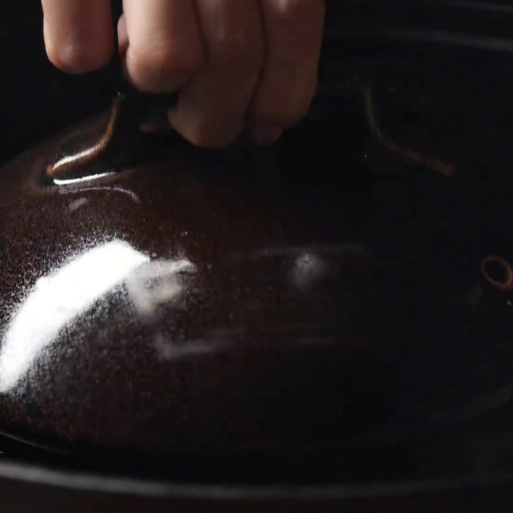 Mano colocando una tapa oscura sobre la sartén para atrapar el vapor y fundir el queso.