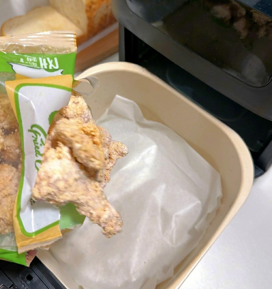 Piezas de pollo empanado congelado cayendo de una bolsa a la cesta de la freidora con papel de horno.
