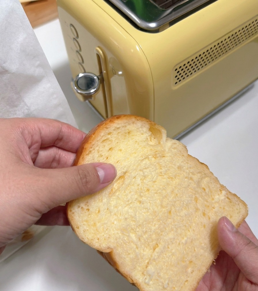 Una persona introduciendo una rebanada gruesa de pan blanco en una tostadora amarilla de estilo retro.