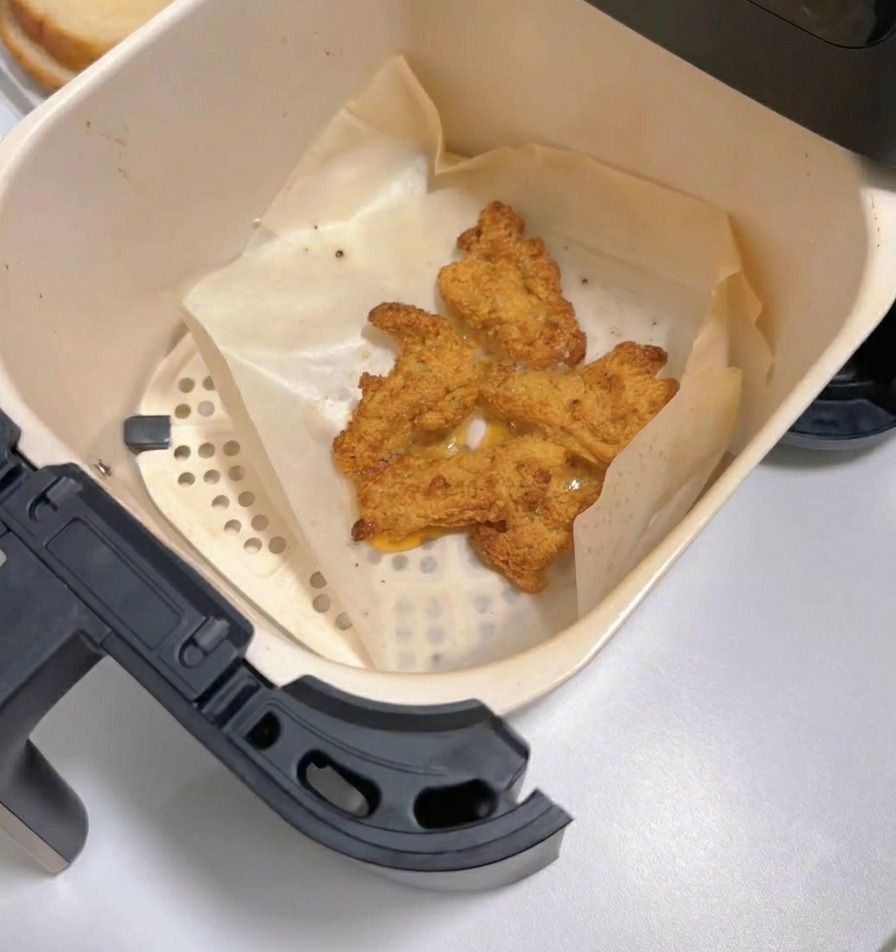 Cesta de freidora de aire abierta mostrando pollo frito dorado y crujiente sobre papel vegetal.