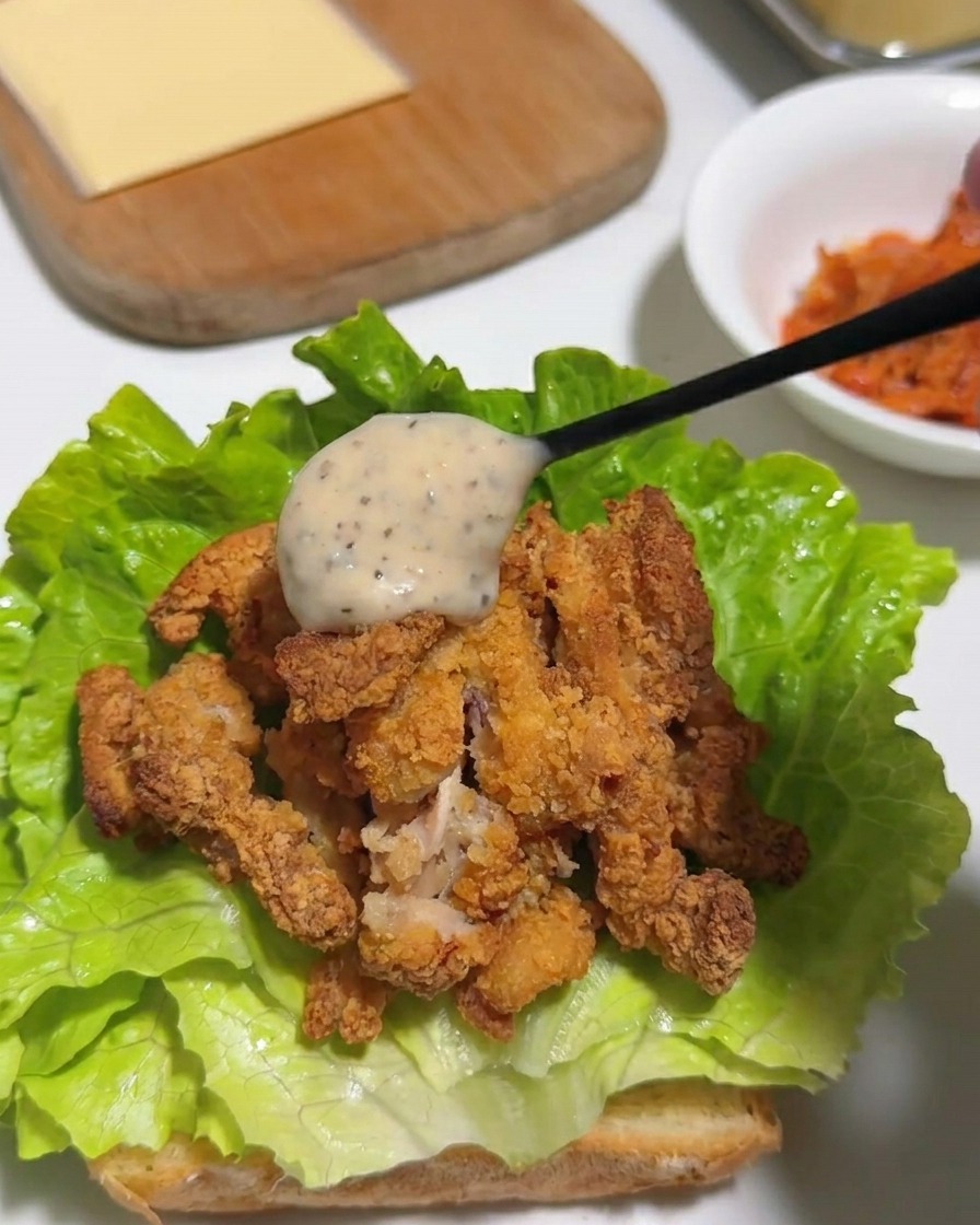 Una cuchara vertiendo mayonesa cremosa de yuzu y pimienta sobre el pollo crujiente.