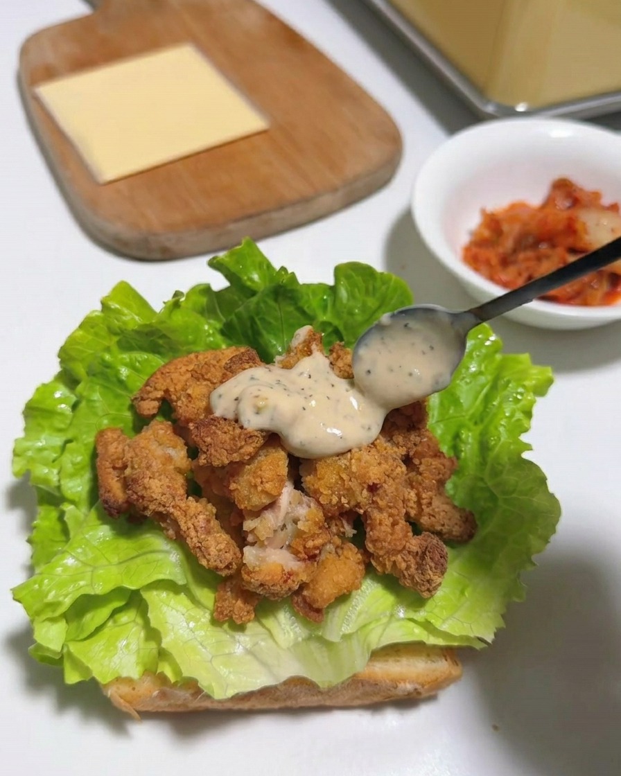 Una loncha de queso amarillo sobre las tiras de pollo con salsa y lechuga.