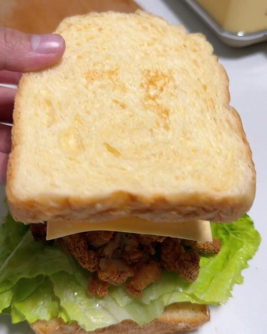 Una mano colocando la segunda rebanada de pan tostado sobre el relleno del sándwich.