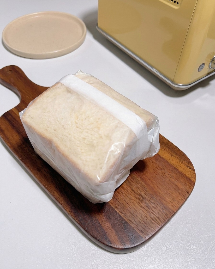 Sándwich grueso envuelto apretadamente en papel vegetal sobre una tabla de madera.