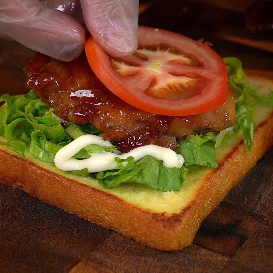 Una mano colocando una rodaja de tomate fresco sobre el pollo glaseado.