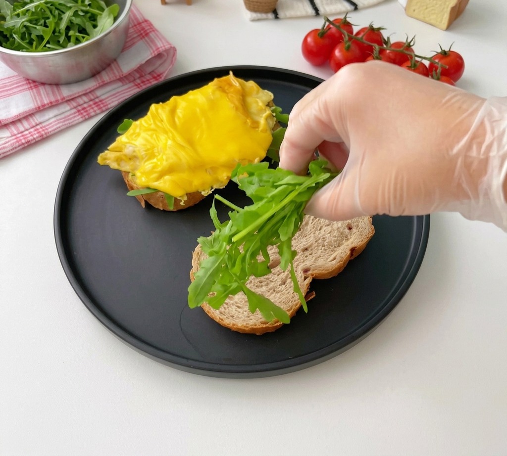 Una mano colocando hojas de rúcula fresca sobre una rebanada de pan tostado.