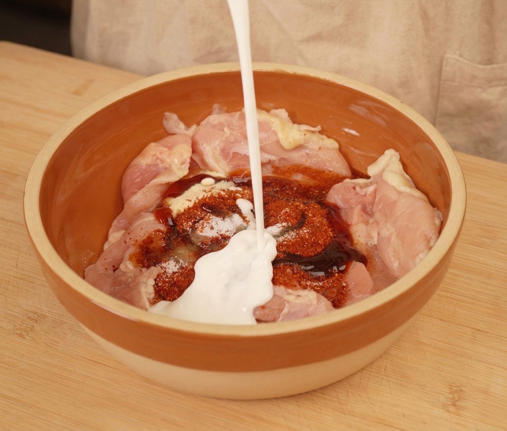 Vertiendo yogur natural sobre los contramuslos de pollo y las especias en un bol.