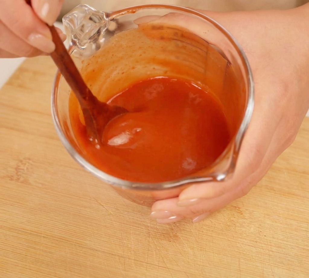 Removiendo una salsa roja espesa en una jarra medidora con una cuchara de madera.