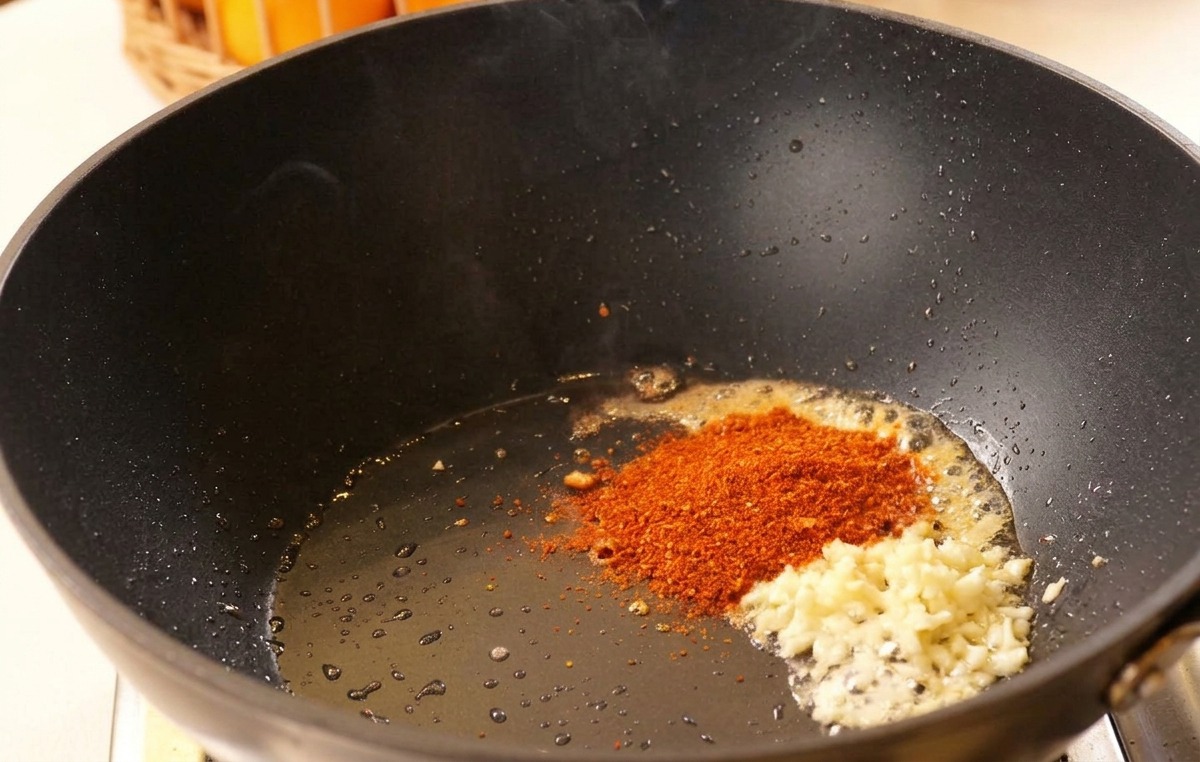 Ajo picado y chile en polvo en aceite caliente dentro de un wok negro.
