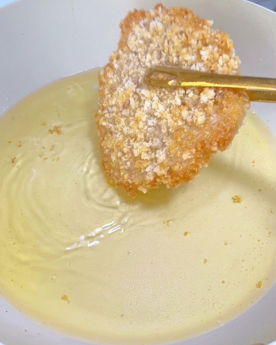 Milanesa de pollo con costra dorada siendo volteada con pinzas en una sartén con aceite.