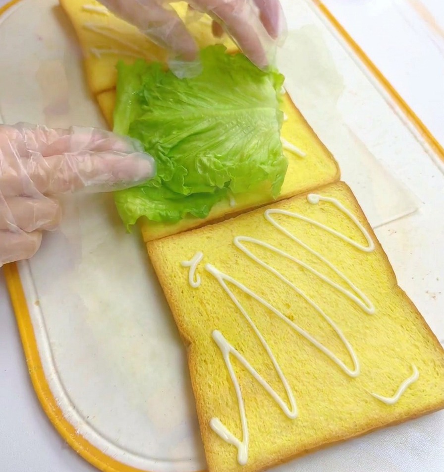 Manos colocando una hoja de lechuga fresca sobre el pan con mayonesa.