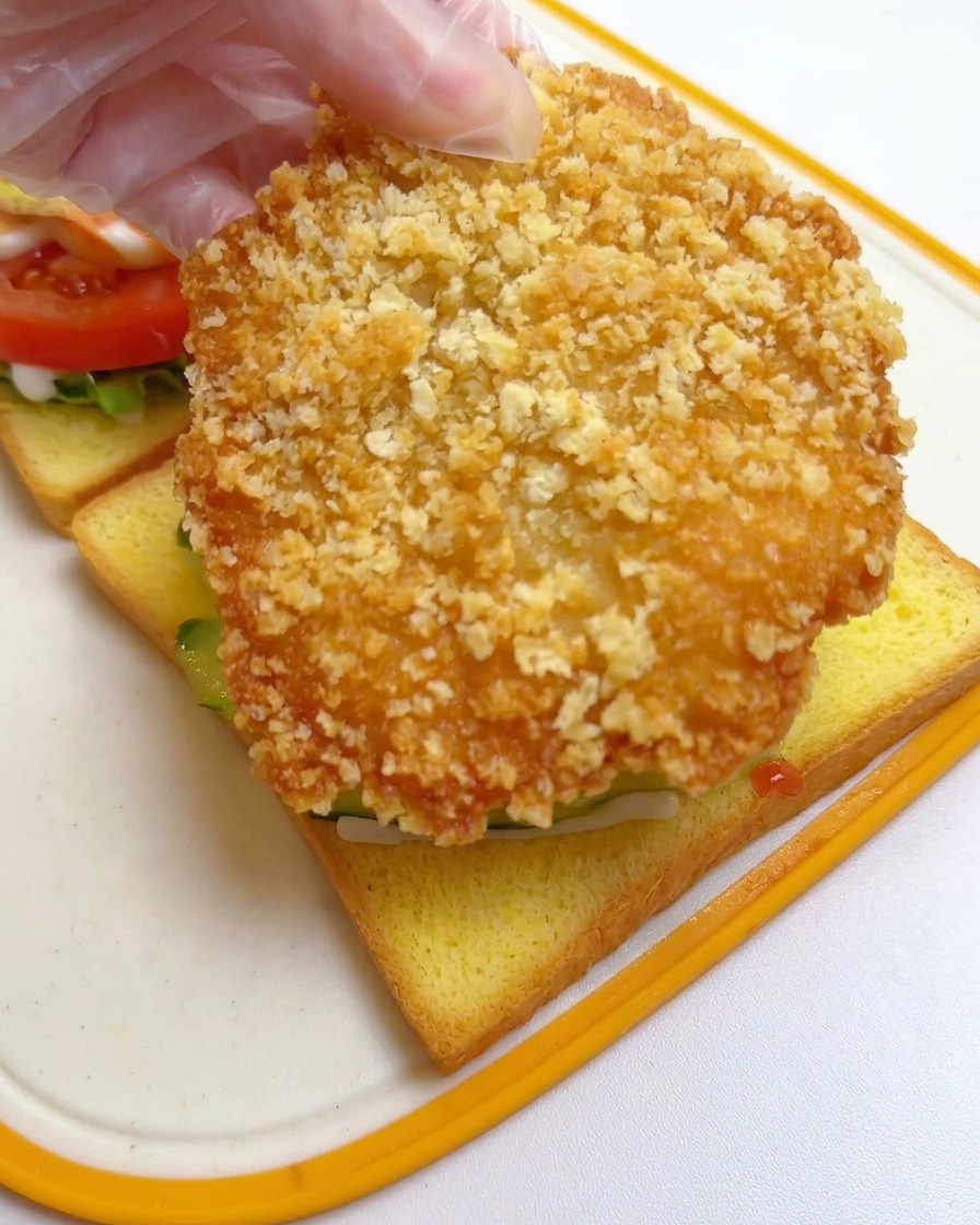 Mano colocando la milanesa de pollo frita y dorada sobre las láminas de pepino.