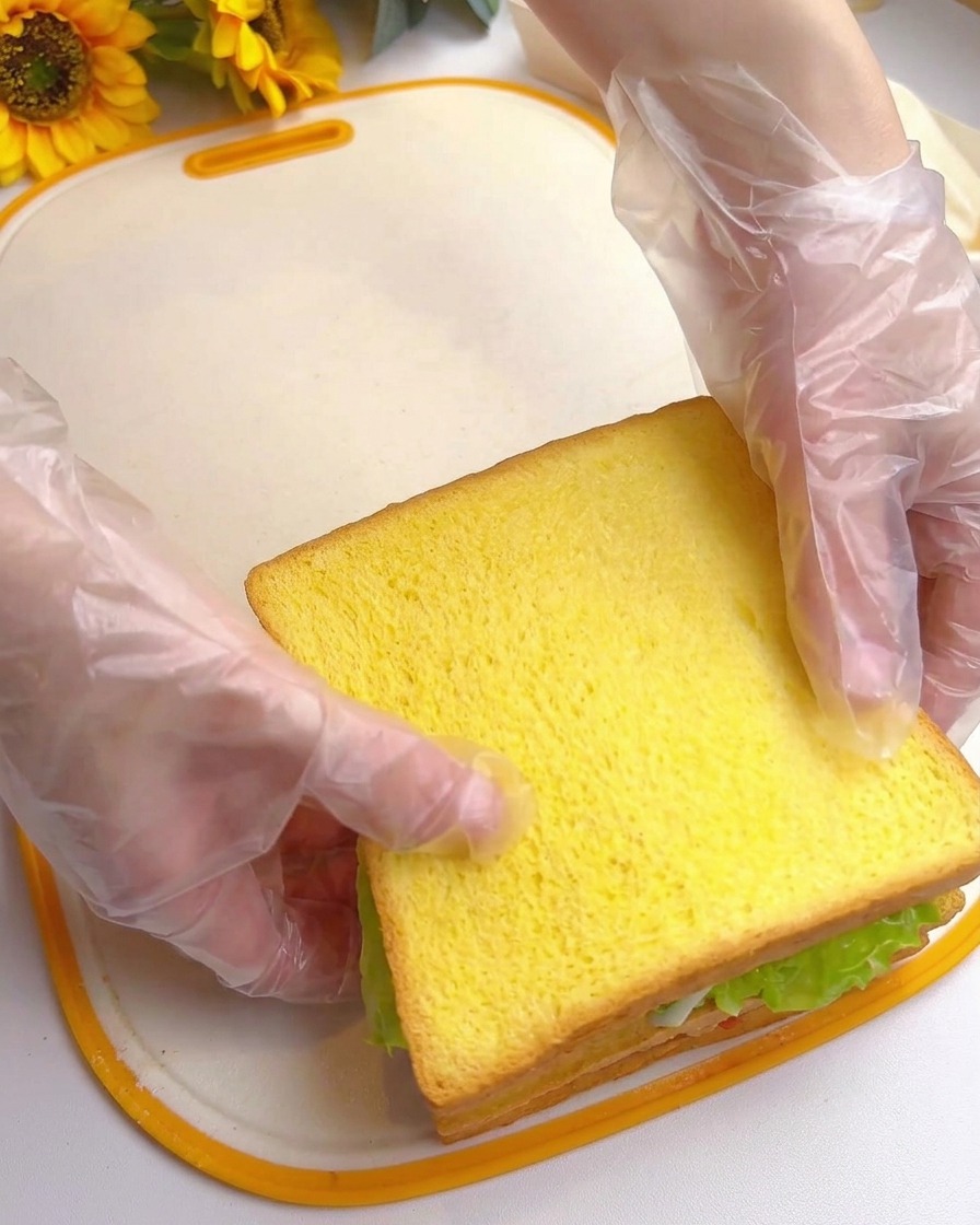 Dos manos presionando la rebanada superior del sándwich para completar el montaje.