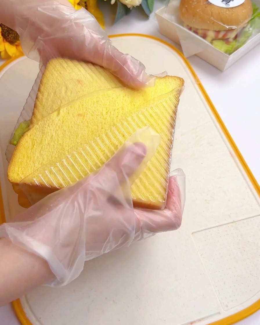 Manos introduciendo el sándwich en un molde plástico triangular transparente.