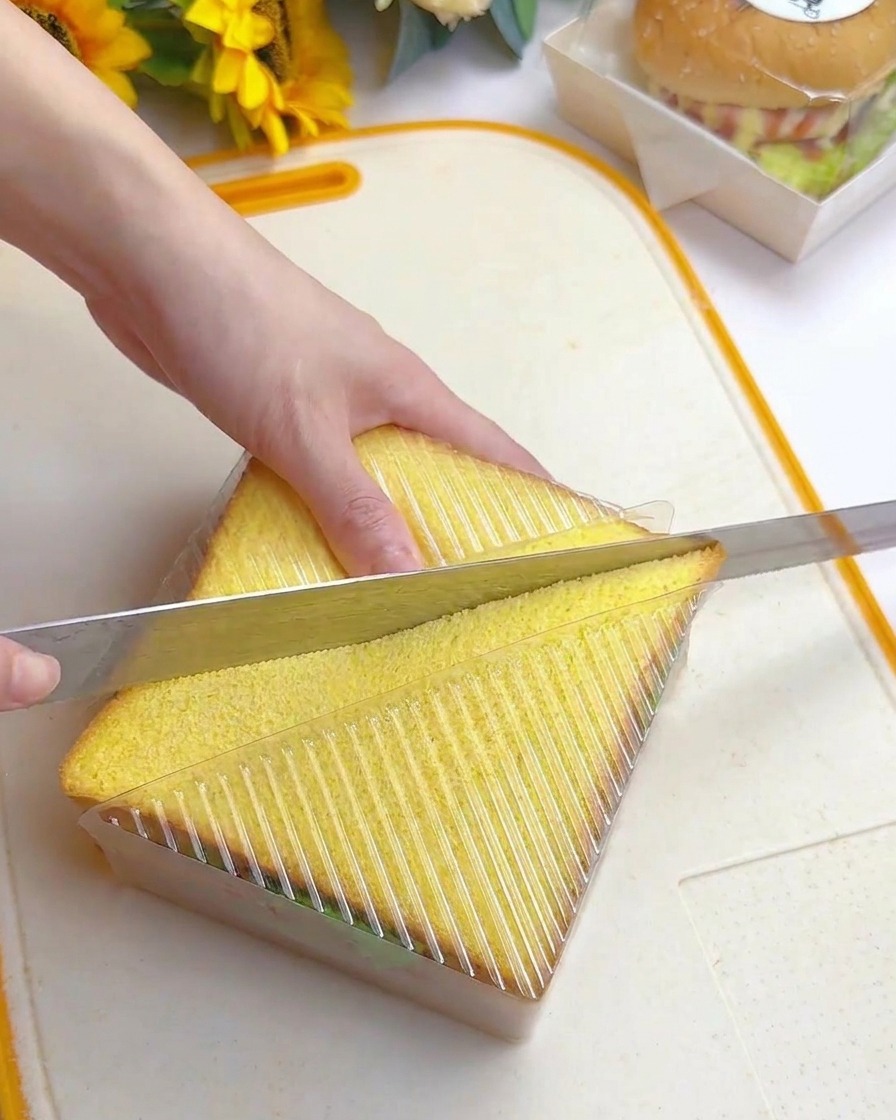 Cuchillo de sierra cortando diagonalmente el sándwich dentro del molde plástico.