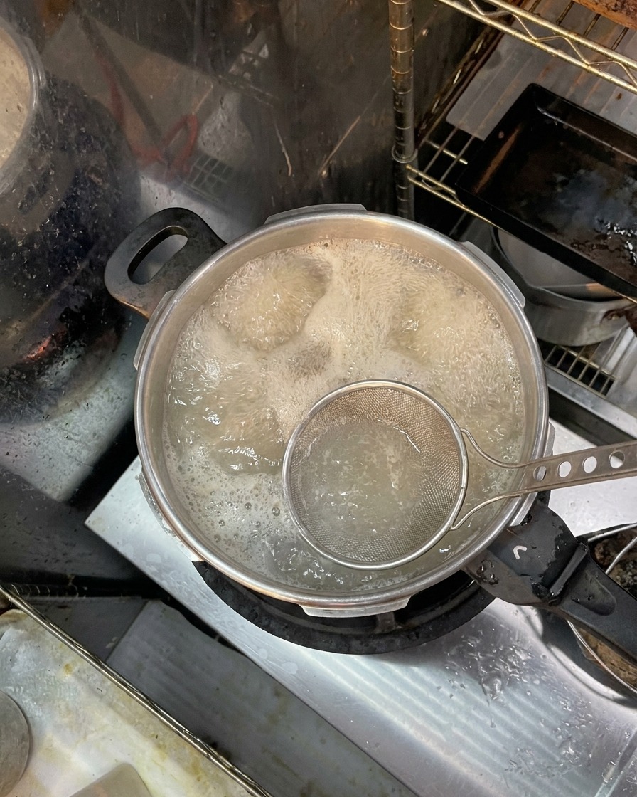 Un espumador metálico recogiendo espuma marrón e impurezas de la superficie del agua hirviendo con huesos.