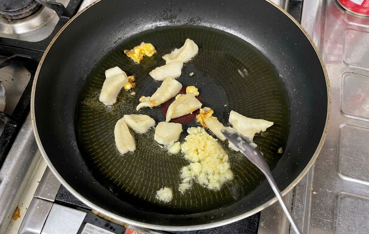 Ajo picado removiéndose con una cuchara junto a trozos de grasa en una sartén con aceite caliente.