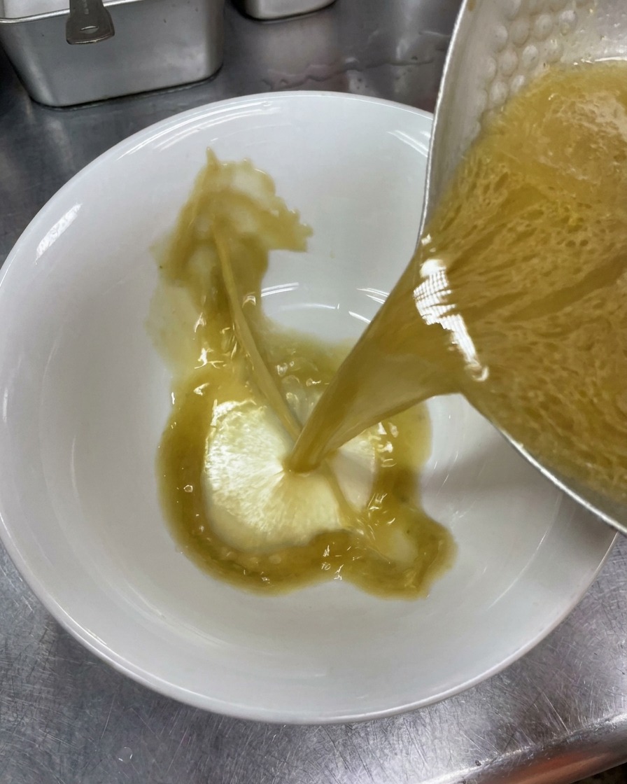 Caldo tonkotsu sazonado y opaco vertiéndose desde una olla metálica en un tazón de cerámica blanca para ramen.