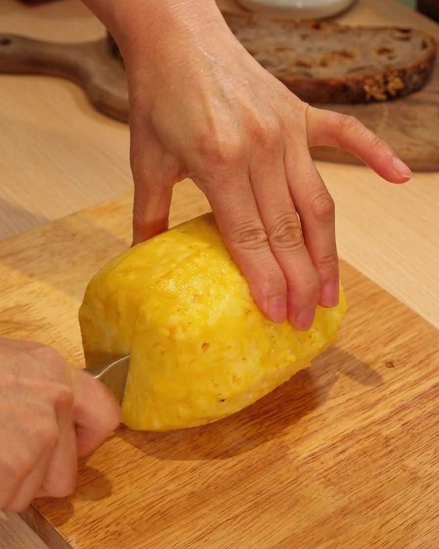 Manos cortando una piña fresca pelada en una tabla de madera.