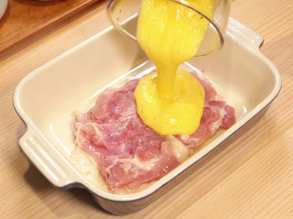 Vertiendo zumo de piña recién triturado sobre un contramuslo de pollo crudo en un plato cerámico.