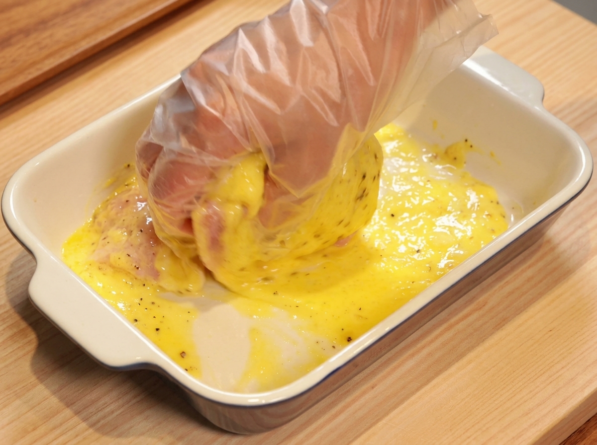 Mano con guante masajeando el pollo crudo con el marinado de piña y especias.