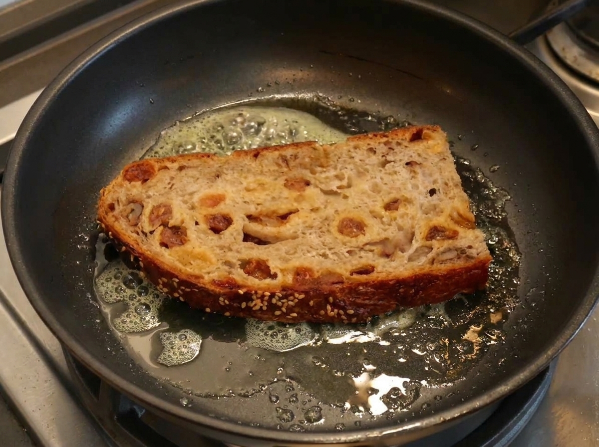 Rebanada gruesa de pan artesano tostándose en una sartén con mantequilla derretida.