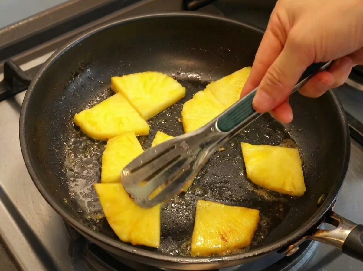 Rodajas de piña dorándose en una sartén caliente con mantequilla.