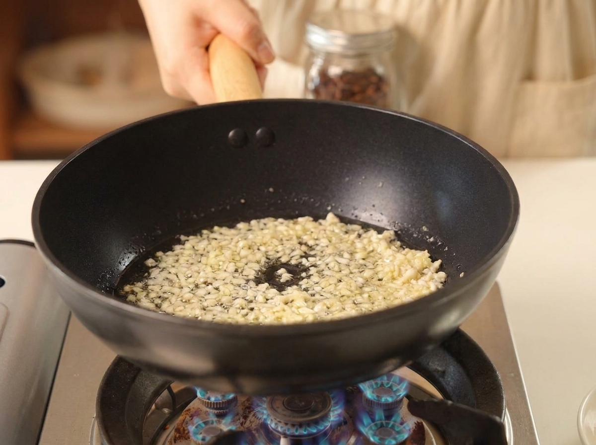 Ajo picado friéndose en una sartén negra con aceite caliente burbujeando.