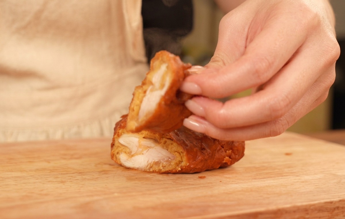 Dedos sosteniendo la mitad de un trozo de pollo frito, mostrando la costra dorada y la carne blanca cocida.