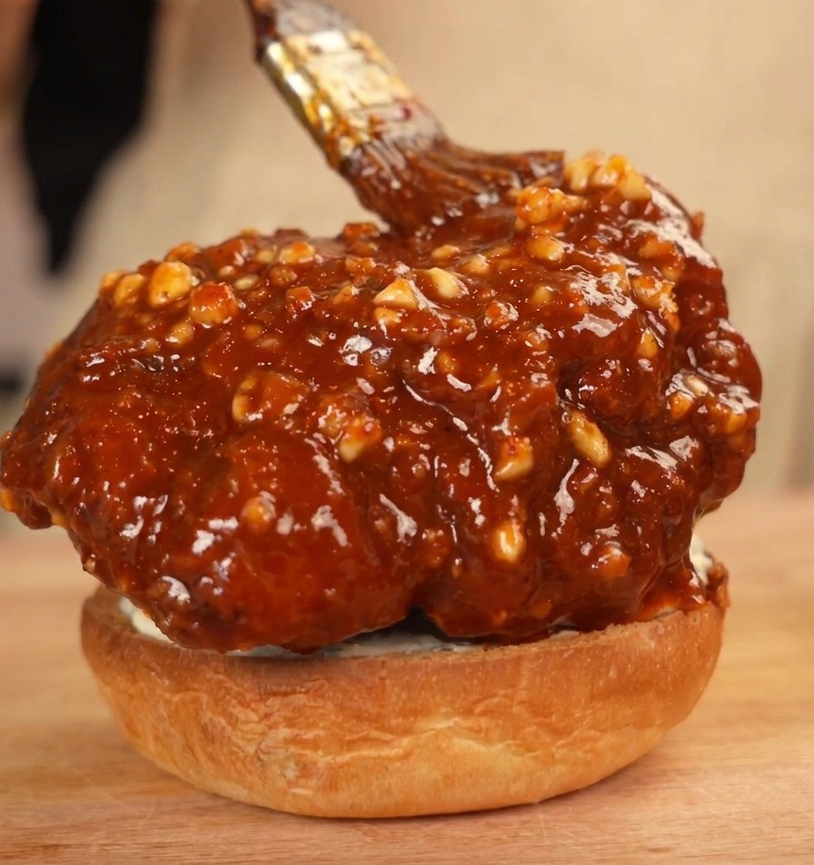 Pollo frito glaseado sobre la base del pan, recibiendo una pincelada extra de salsa de cacahuete y chile.
