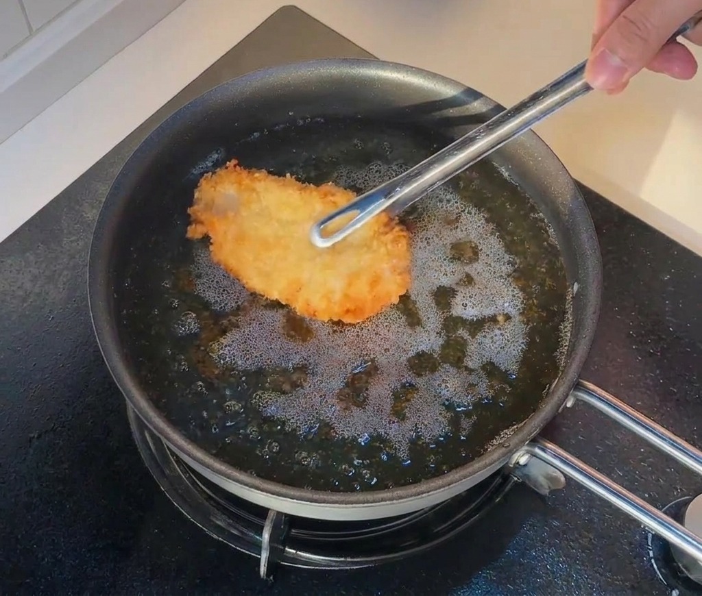Pinzas introduciendo de nuevo el pollo frito en aceite muy caliente para una segunda fritura.