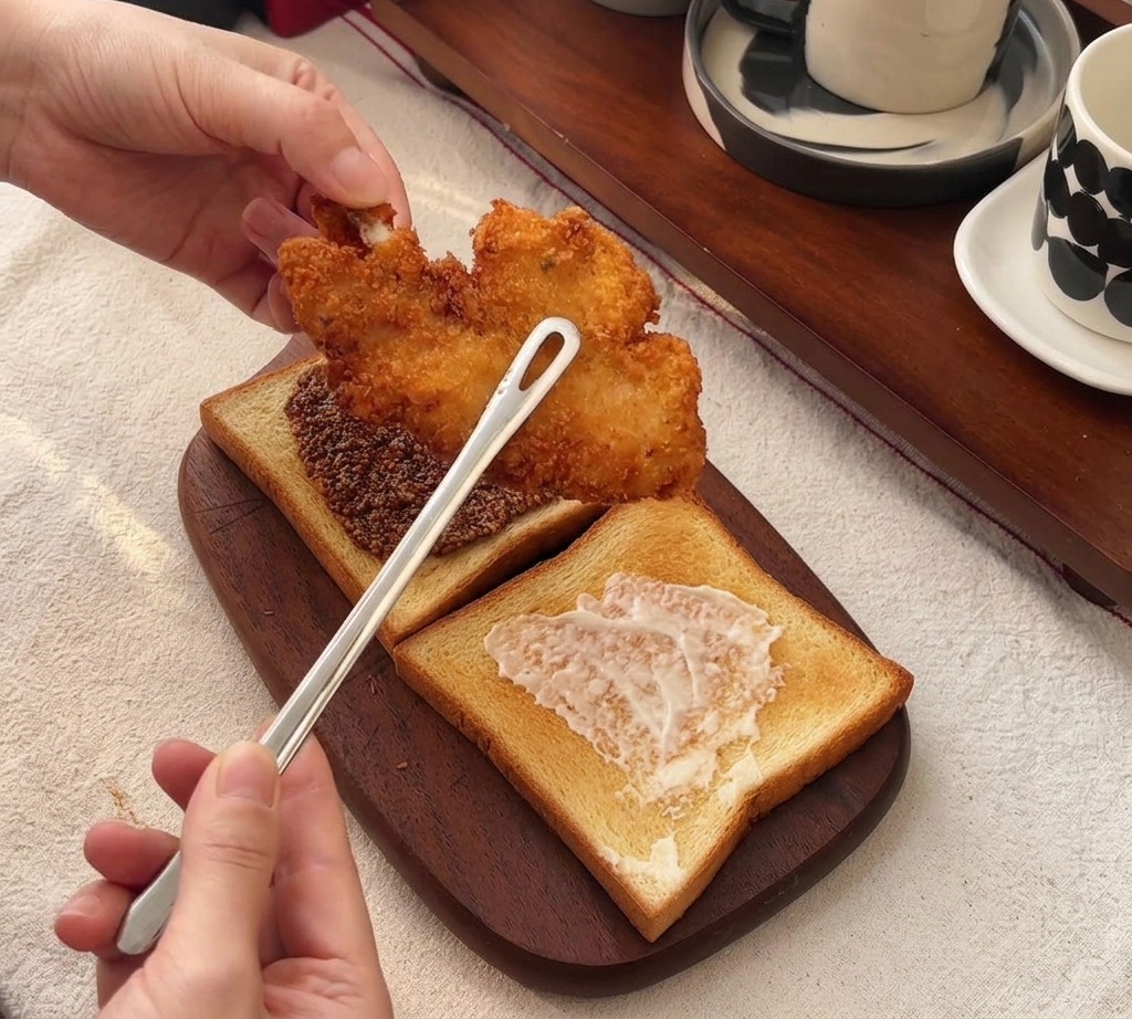 Pinzas colocando un filete de pollo frito grande y crujiente sobre pan tostado con miel y mostaza.