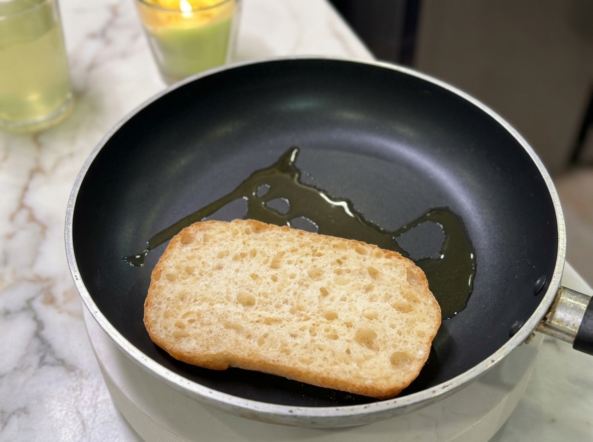 La mitad de un pan ciabatta tostándose en una sartén plana con un chorrito de aceite vegetal.