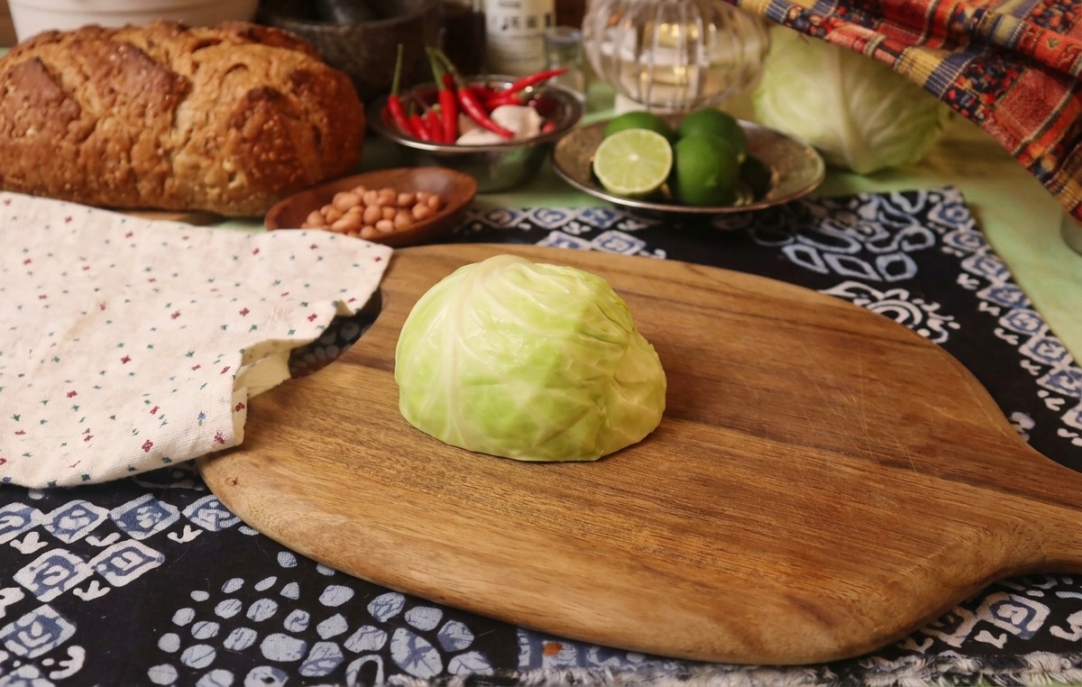 Una pieza de col verde fresca sobre una tabla de cortar de madera junto a un paño rústico.