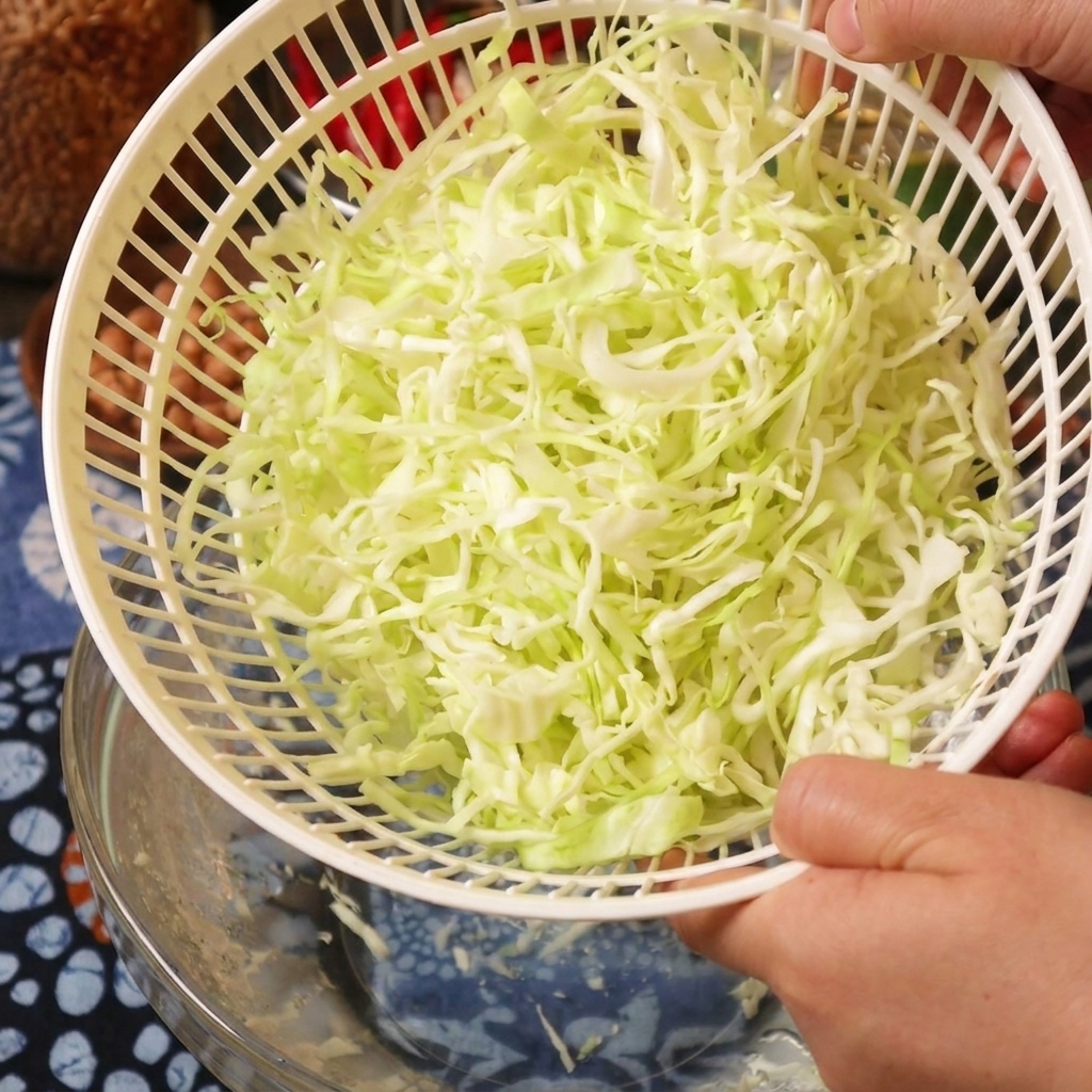 Una persona sosteniendo una cesta de centrifugadora de verduras blanca llena de col rallada recién seca.