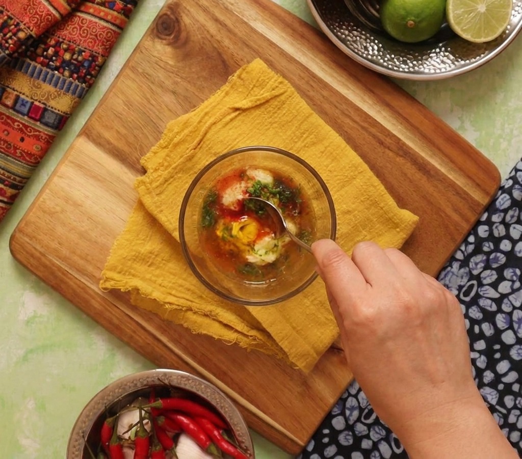 Una mano removiendo un bol de salsa naranja cremosa hecha con mayonesa, lima y especias.