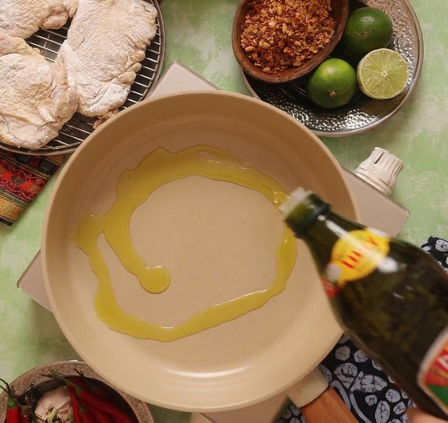 Aceite de oliva vertiéndose en una sartén cerámica beige colocada sobre un hornillo portátil.