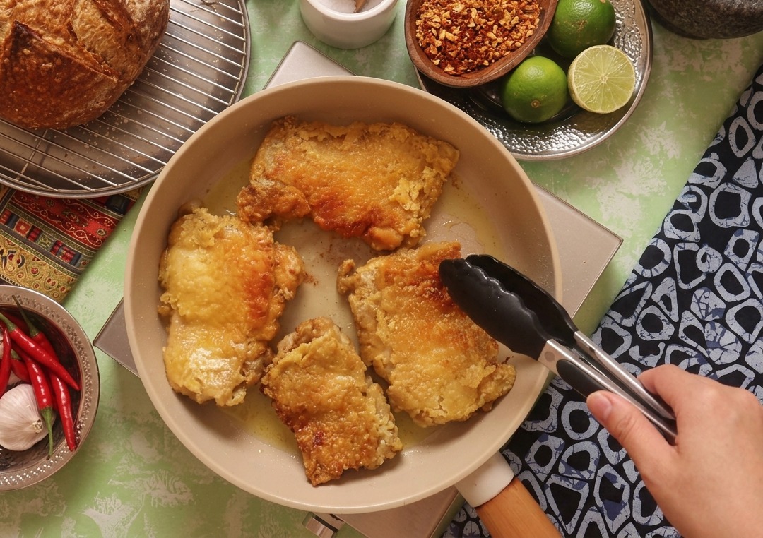 Pinzas de cocina girando el pollo en la sartén, mostrando una superficie frita perfectamente dorada y crujiente.