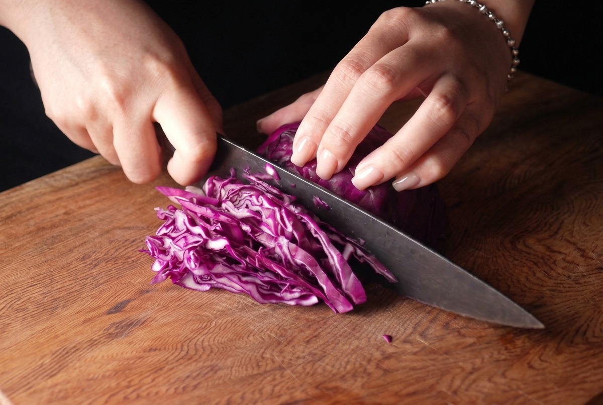 Una persona cortando finamente un repollo morado con un cuchillo de chef en una tabla de madera.